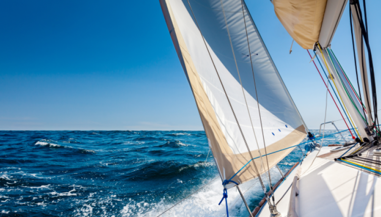 Imbarcazione a vela naviga nel mare con cielo azzurro sullo sfondo.